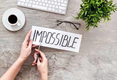 All is possible concept. Hands cut word impossible on grey office desk.