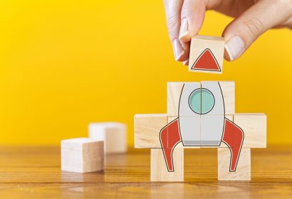 Hand arranging wooden cubes in a structure rocket shape. Conceptual of business startup and strategy.